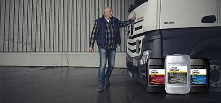 Lorry driver tapping the front of his lorry in a warehouse with Mobil Delvac Modern, Legend and Ultra packs in front