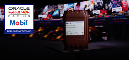 A brown Mobil oil container on a podium with an Oracle Red Bull Racing logo and blurred pit/garage scene in the background.